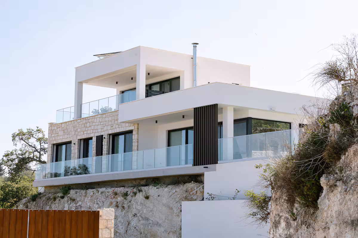 Exterior of the two-level white villa with stone cladding and glass balustrades on the hillside in Fyti