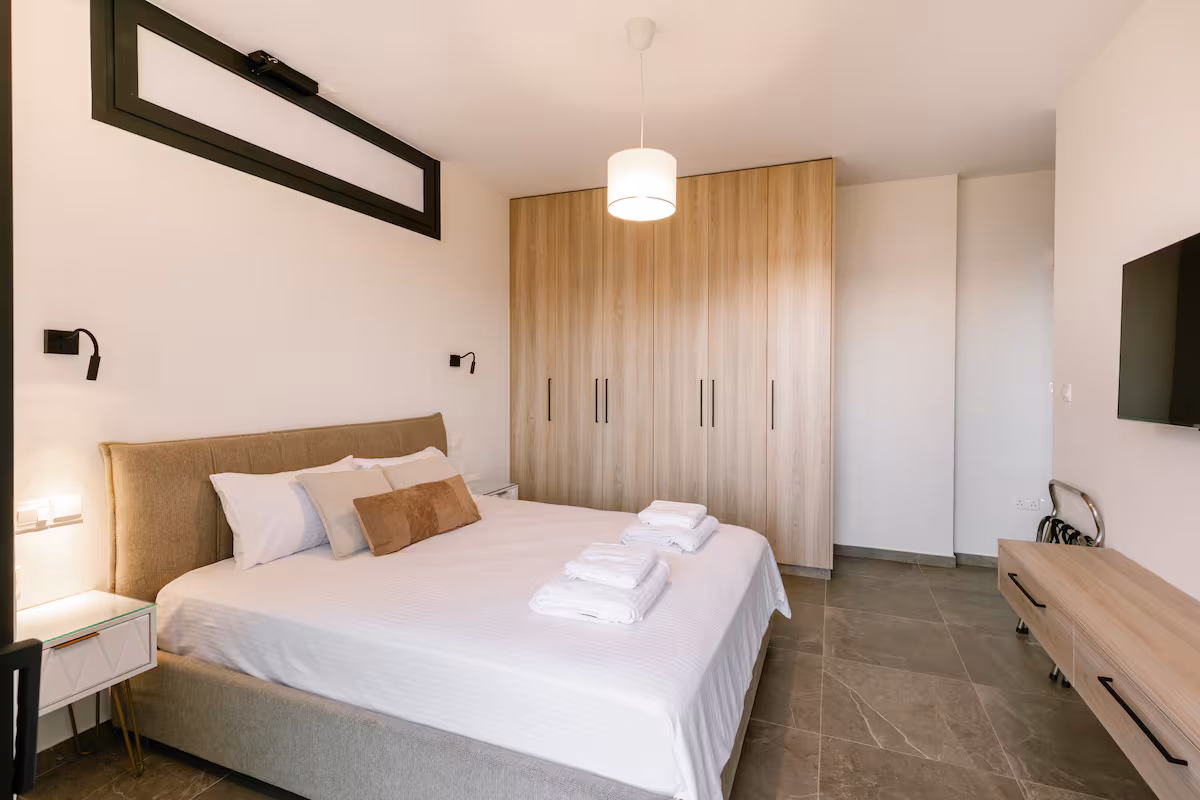 Bedroom with a double bed, wooden wardrobes and a wall-mounted TV